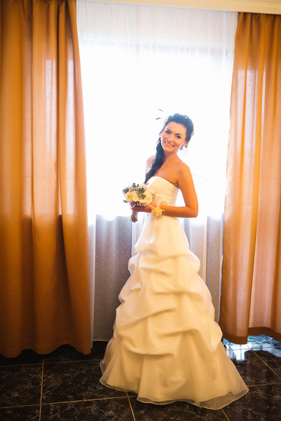 όμορφη νεαρός ευτυχισμένη νύφη που στέκεται κοντά στο παράθυρο - Φωτογραφία, εικόνα