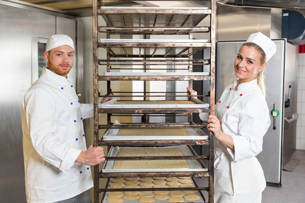 Two bakers posing with shelf containing pastry in bakery - Фото, изображение