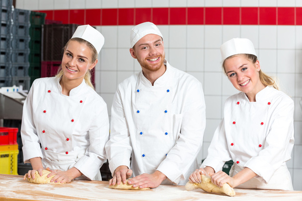 Three bakers in bakery kneading fresh dough - Foto, afbeelding