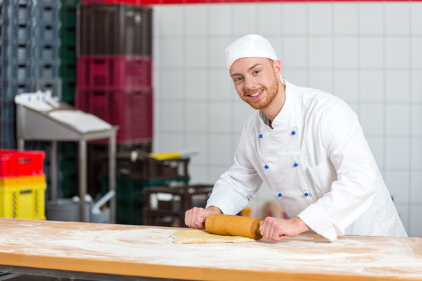 Baker with dough roll working in a bakery - Фото, изображение