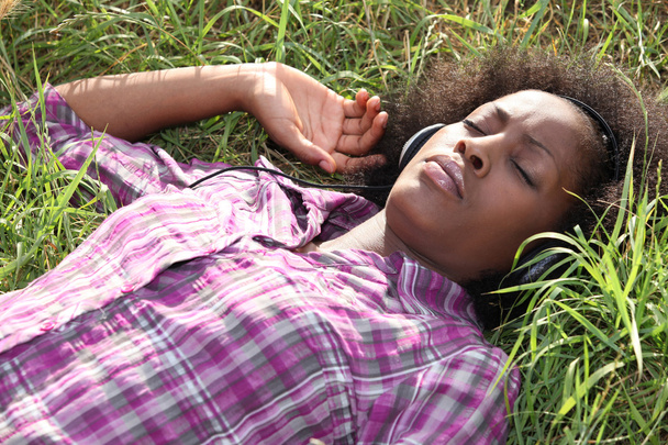Woman lying in field listening to music - Foto, imagen