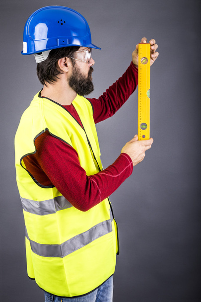 Young engineer with hardhat and reflective vest holding a levele - Valokuva, kuva