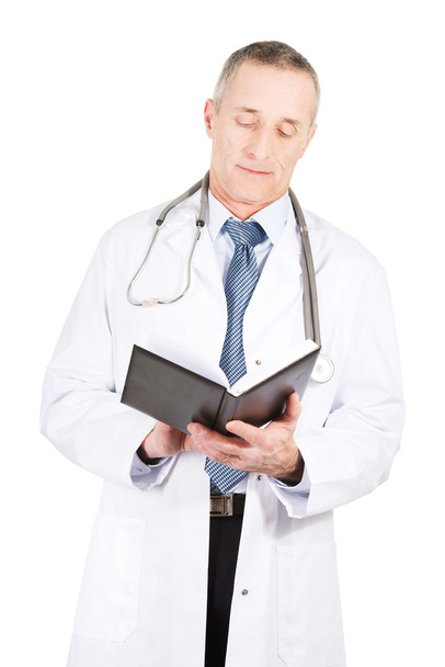 Mature male doctor reading notes - Foto, afbeelding