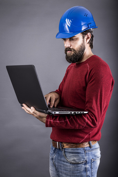 Young engineer with hardhat standing while working on his laptop - Foto, immagini