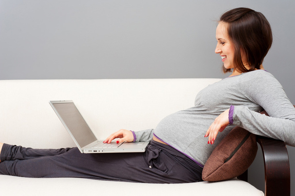 Donna incinta sorridente con computer portatile
 - Foto, immagini