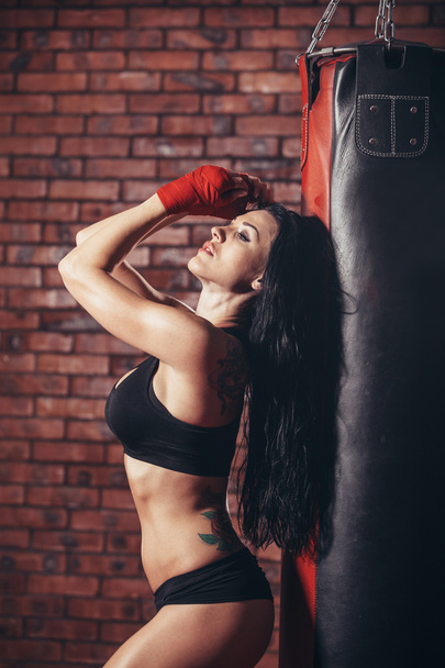Young beautiful sexy boxer woman with red boxing bandage on hands. punching bag.  the background wall of brick. - Foto, immagini