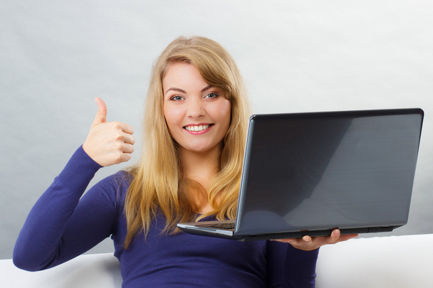 Gelukkige vrouw met behulp van laptop zittend op de Bank en het tonen van duimen omhoog - Foto, afbeelding