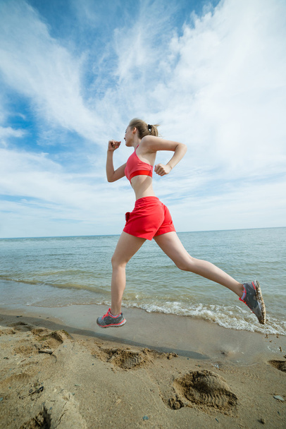 Young lady running at the sunny summer sand beach. Workout.  Jog - Photo, Image