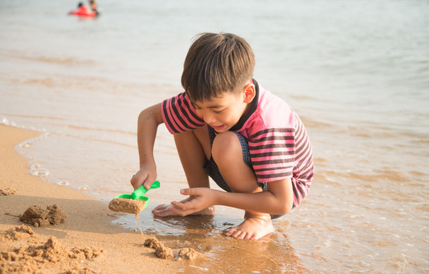 Menino brincando de areia na praia hora de verão
 - Foto, Imagem