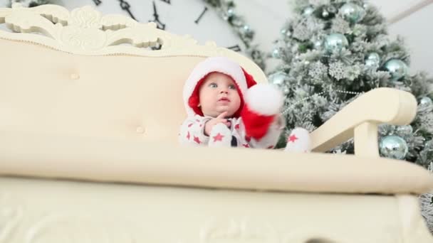 baby sits near a Christmas tree with a gift - Záběry, video