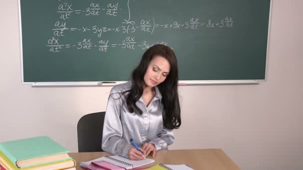 Meisje zit aan tafel en pishit in een notitieblok, opstaat en loopt uit de klas. - Video