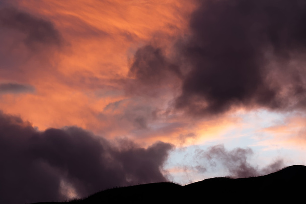 θυμωμένος σύννεφα στο ηλιοβασίλεμα ενάντια στο βουνό σιλουέτα - Φωτογραφία, εικόνα