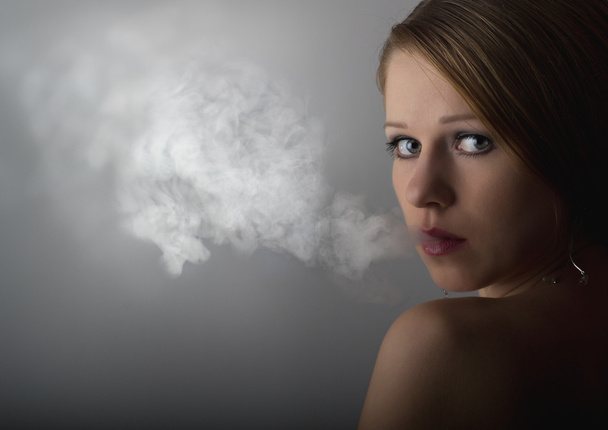 Beautiful young woman with cigarette smoke on a dark gray backgr - Photo, Image