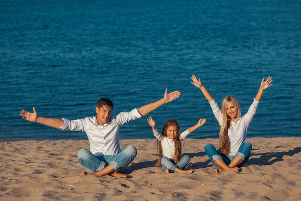 Familie op het strand. Lotus houding. handen omhoog, geluk, jeans. - Foto, afbeelding