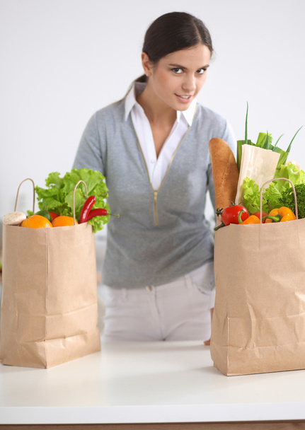 Молода жінка тримає продуктовий сумку з овочами стоїть на кухні
 - Фото, зображення