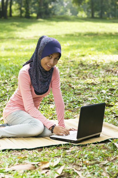 mooie jonge moslim dame zit op de mat met laptop - Foto, afbeelding