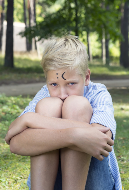trauriger Junge umarmt ihre Knie und sitzt auf grünem Gras in der Natur. con - Foto, Bild