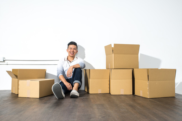 A yong asian man sitting on floor smiling with boxes - Foto, Imagem