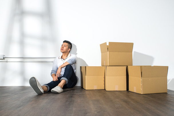 A yong asian man sitting on floor with boxes - Фото, изображение