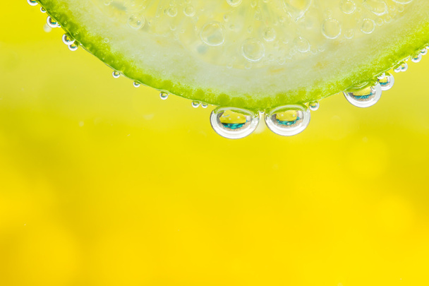 grüne Limette mit Wasserspritzer. gelber Hintergrund. - Foto, Bild