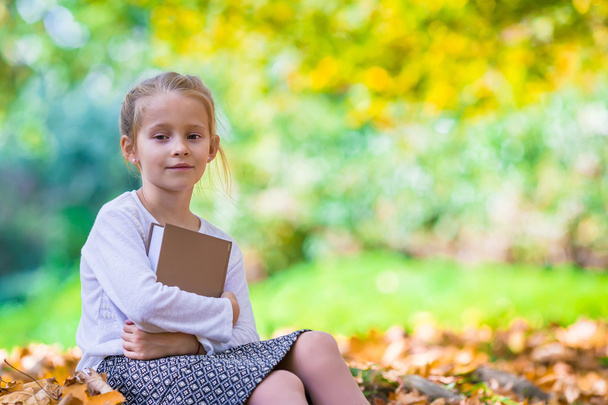 Очаровательная маленькая умная девочка с книгой в красивом осеннем дау на открытом воздухе
 - Фото, изображение