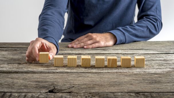 Front view of a man placing eight blank wooden cubes in a row - Photo, Image