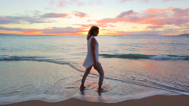 夕日を楽しんで幸せな年上の女性がビーチを散歩します。. - 映像、動画