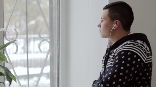 man listens to music with headphones and looking out the window - Materiał filmowy, wideo