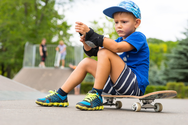 Little boy putting on elbow pads at the skate park - Zdjęcie, obraz