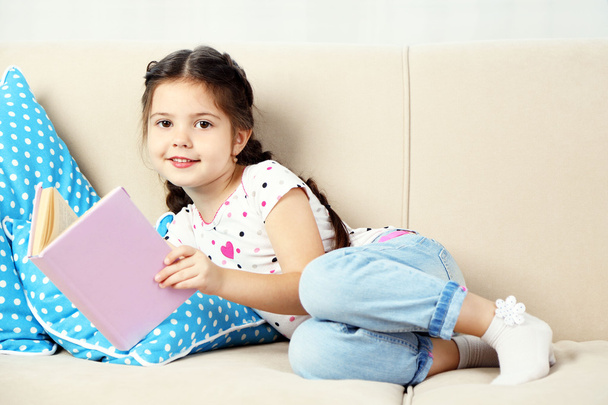 Little girl sitting on sofa with book - Foto, immagini