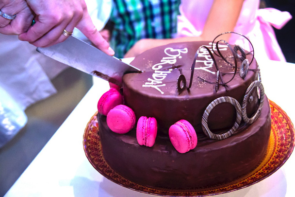 Κοπή το όμορφα διακοσμημένο μια εορταστική κέικ σοκολάτας με την επιγραφή χαρούμενα γενέθλια σε κομμάτια - Φωτογραφία, εικόνα