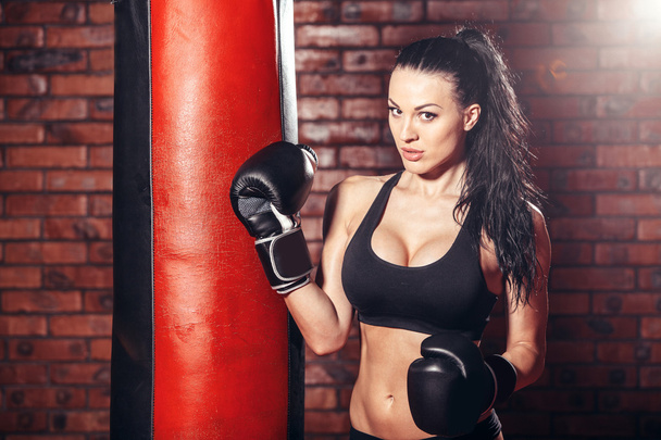 Young sexy girl with boxing gloves, punching bag, on the background wall of red brick. - Foto, immagini