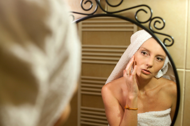 Женщина средних лет проверяет лицо в зеркале ванной после сё
 - Фото, изображение