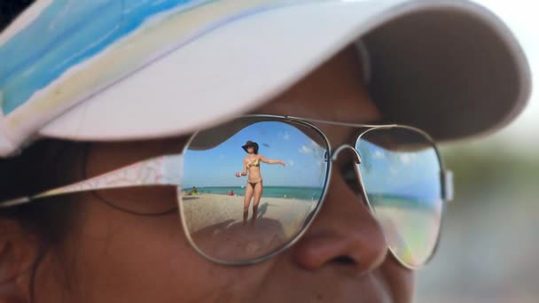 Woman looking at another womand dancing on beach through her sunglasses - Footage, Video