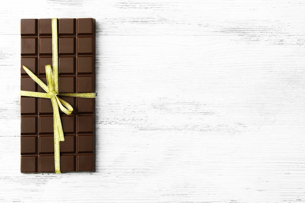 Milk chocolate bar with colorful bow on color wooden background - Foto, Imagem