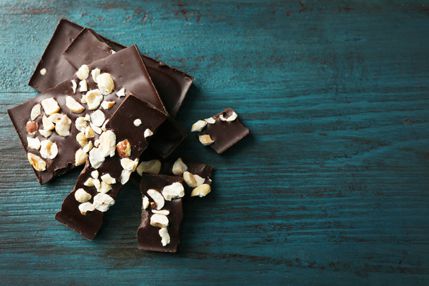 Black chocolate pieces with nuts on color wooden background - Foto, Imagem