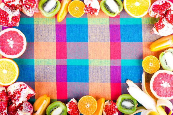 Frutas frescas en una toalla de cocina a cuadros de colores. Marco alimenticio crudo y vegetariano. Naranja en rodajas, caqui, kiwi, mandarina, plátano, limón, manzana, pomelo, granada, lima, Vista superior
 - Foto, imagen