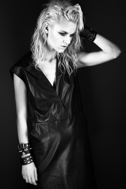 Daring girl model in black leather dress, style of rock, dark make-up, wet hair and bracelets on her arms. - Fotó, kép