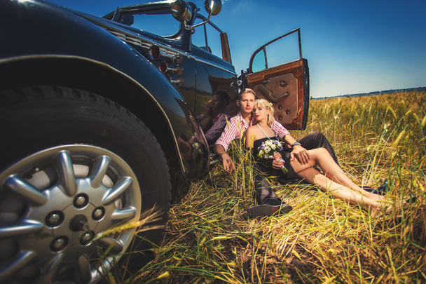 Happy couple sitting near car on field - Foto, imagen