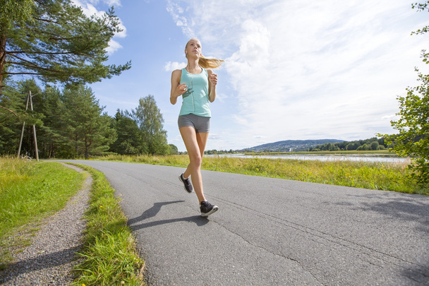 Mulher motivada corre rápido em uma estrada na floresta
 - Foto, Imagem