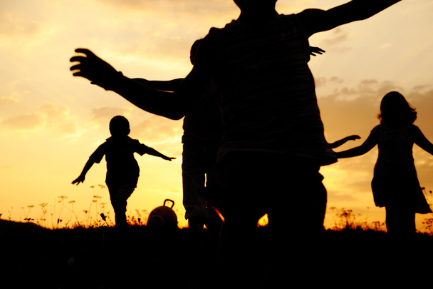 Silhouette, group of happy children playing on meadow, sunset, summertime - Fotó, kép