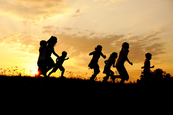 Silhouette, group of happy children playing on meadow, sunset, summertime - Photo, Image