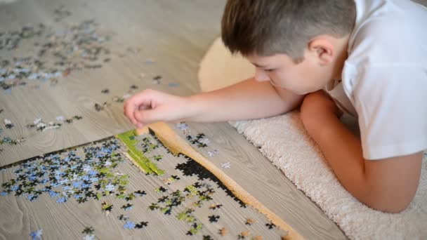 teenager boy collects puzzles  lying on  floor - Video, Çekim