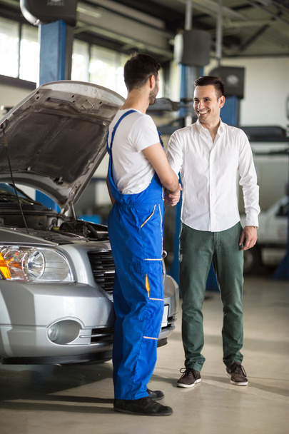 smiling auto mechanic and client shaking hands - Foto, afbeelding