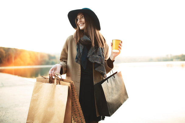 Ελκυστικό χαριτωμένο κορίτσι με τις τσάντες αγορών και ζεστό ποτό στο χέρι - Φωτογραφία, εικόνα
