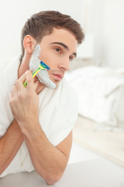 Attractive guy shaves with joy in bathroom - Fotografie, Obrázek