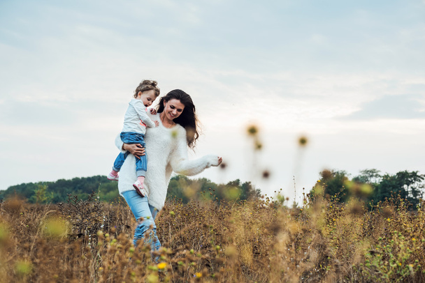mother and daughter playing on autumn field together, loving family having fun outdoors - Foto, afbeelding