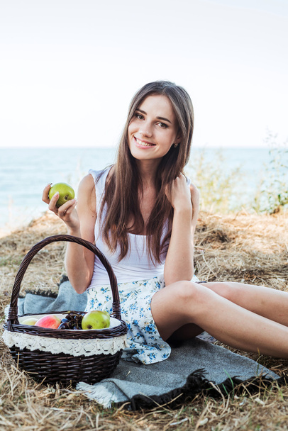 young caucasian female on seaside with basket with fruits. Girl eating fruits, healthy eating and healthy living concept - Foto, Imagen