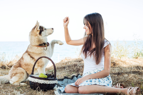 young caucasian female and red siberian husky dog on seaside with basket with fruits. eating fruits, healthy eating and healthy living concept - Fotó, kép
