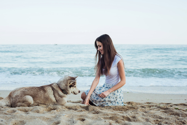 young caucasian female playing and having fun with siberian husky dog on beach - Photo, Image